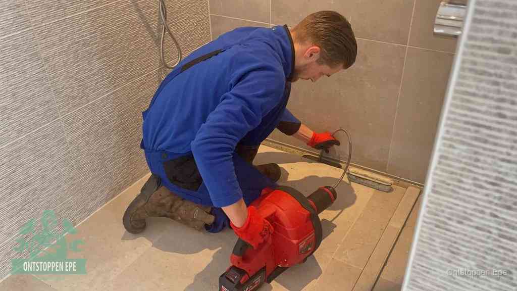 Een monteur ontstopt een langwerpige douchegoot met een elektrische veer, een doucheputje verstopt door haren en zeep in Epe