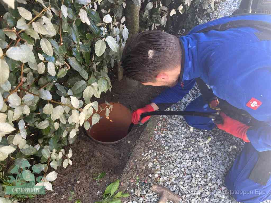 Een monteur voert een slang in een geopende rioolput in de tuin om het hoofdriool te ontstoppen in Epe
